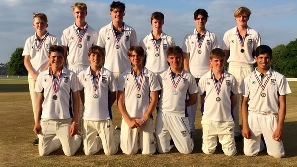 Un grupo de estudiantes de la Canford School está en uniforme de cricket en un campo de césped bajo un cielo despejado.