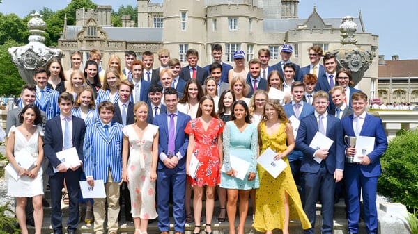 Un gran grupo de personas vestidas de manera formal está frente al edificio del castillo de la Canford School para una foto grupal.