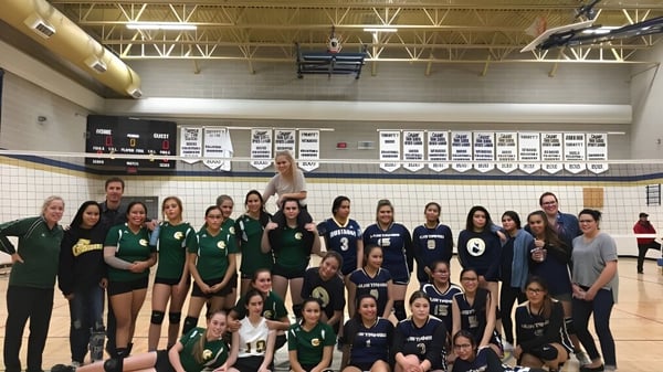 Un grupo de estudiantes de la Canmore Collegiate High School posan en ropa deportiva en el gimnasio frente a equipos deportivos y pancartas.
