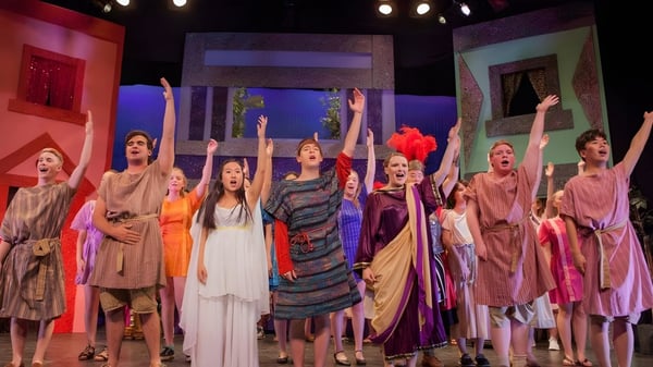 Estudiantes de Canterbury School realizan una actuación dinámica en el escenario con trajes coloridos.