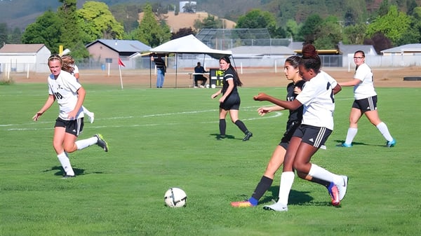 Estudiantes de la Canyonville Academy juegan un partido de fútbol en el campo deportivo verde.