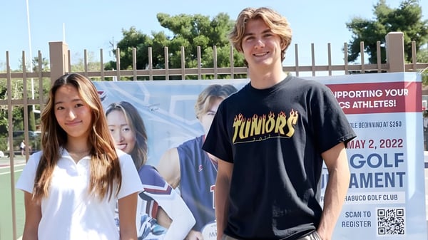 Dos estudiantes están frente a un cartel para un evento de golf en el campus de la Capistrano Valley Christian.