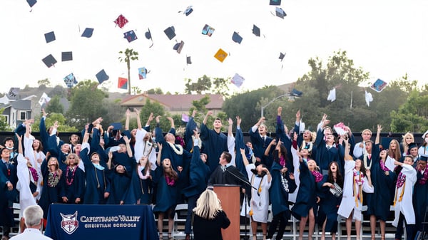 Los graduados de la Capistrano Valley Christian School celebran su graduación frente a palmeras y edificios escolares.