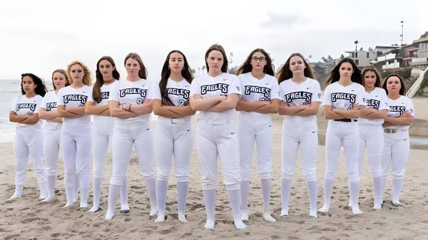 Un grupo de estudiantes en uniformes blancos con el logo de Eagles está en la playa bajo un cielo nublado en el campus de la Capistrano Valley Christian.