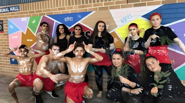 Un grupo de estudiantes de Cardiff High School está frente a un colorido mural en una pared de ladrillo.