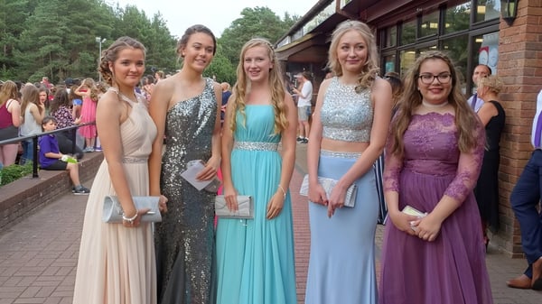 Un grupo de alumnas del Carmel College está vestida de manera formal frente a un edificio de ladrillo en un evento ceremonial.