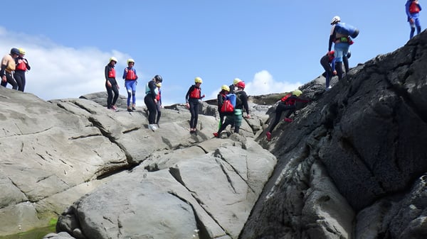Estudiantes de la Carrick on Shannon Community School escalan con equipo colorido en un terreno rocoso bajo un cielo despejado.