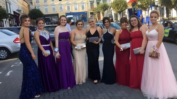 Un grupo de jóvenes mujeres vestidas de gala está en la calle frente al Carrignafoy Community College.