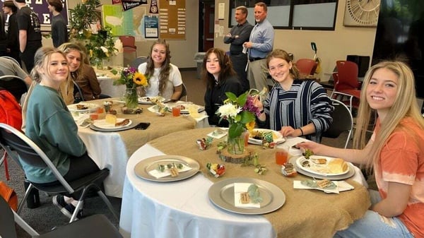 Estudiantes de la Cascade Christian High School están sentados juntos en una mesa comiendo en un ambiente festivo.