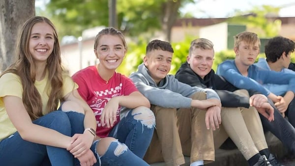 Un grupo de estudiantes de la Cascade Christian High School está sentado al aire libre frente a árboles y áreas verdes.