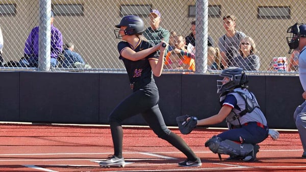 Un jugador de softball en uniforme negro está en el campo de la Cascade Christian High School con un receptor en uniforme azul detrás de la base local.
