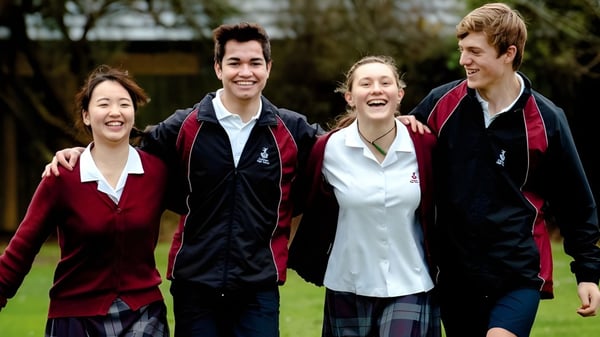 Un grupo de estudiantes está en el campus de la Cashmere High School al aire libre en un prado con árboles de fondo.