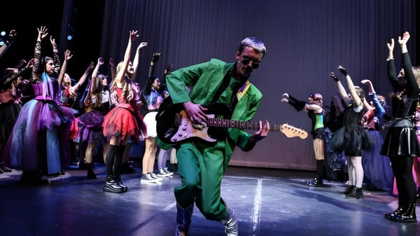 Un músico vestido de verde toca en el escenario frente a un grupo de baile en el campus del Castlepollard Community College.