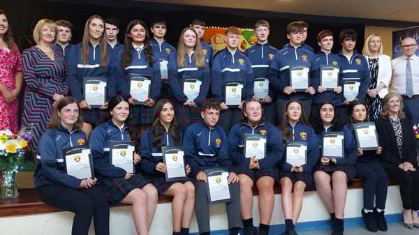 Estudiantes de la Castlerea Community School visten uniformes y sostienen premios en un marco formal.