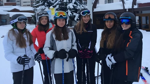 Un grupo de jóvenes alumnas de la Caterham School lleva ropa de deportes de invierno y está en un área exterior nevada con edificios al fondo.