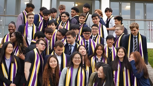 Un grupo de estudiantes de la Caterham School está en ropa de graduación frente a un edificio con grandes ventanas.