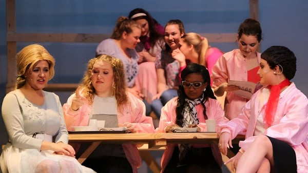 Estudiantes de la Cathedral Preparatory School están sentados en un círculo de grupo alrededor de una mesa frente a un fondo con cielo azul.