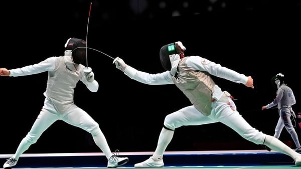 Dos estudiantes de la Cathedral School of St Anne & St James en una competencia de esgrima frente a un fondo oscuro.
