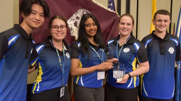 Un grupo de estudiantes de la Cathedral School of St Anne & St James está junto frente a un fondo rojo y blanco en un evento.