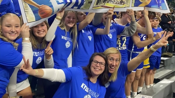 Estudiantes de la Catholic Central High School animan y celebran en el área deportiva con pancartas de fondo.