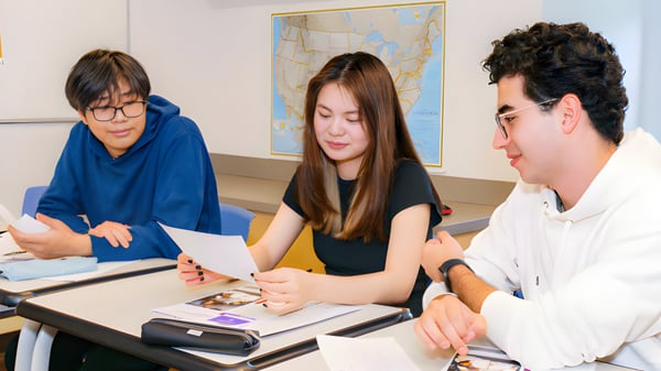 Tres estudiantes están sentados juntos en un escritorio en el aula de la CATS Academy Boston.