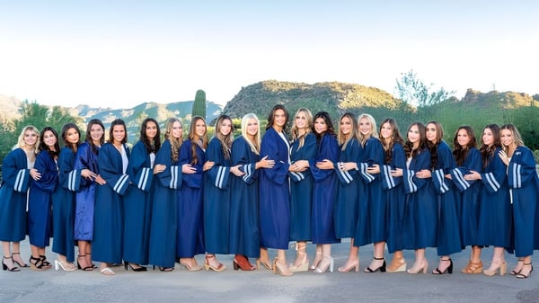 Estudiantes del Cave Creek Unified School District posan en togas de graduación azules frente a un paisaje montañoso.