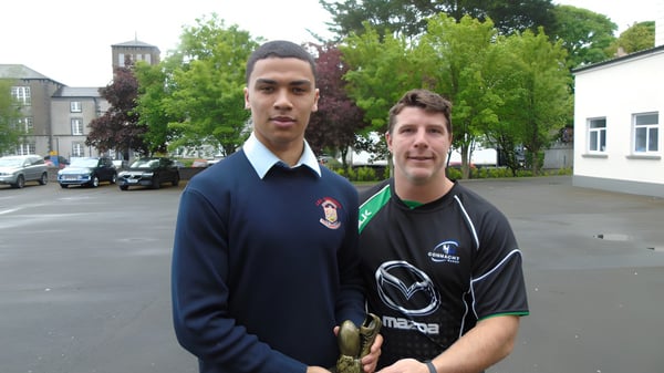 Dos estudiantes de la C.B.S. Roscommon están al aire libre con árboles y edificios de fondo.