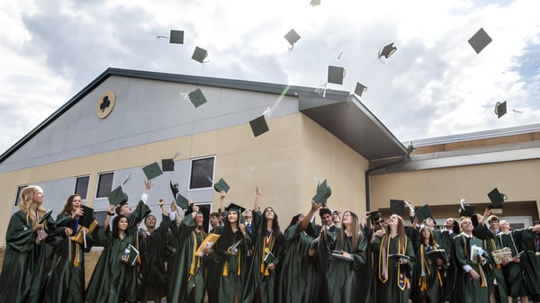 Un grupo de graduadas y graduados de la Centenary Heights State High School celebra su graduación frente al edificio escolar.