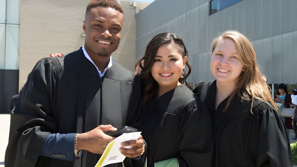 Tres graduados en togas académicas celebran su graduación frente a un moderno edificio del Centennial Collegiate Vocational Institute.