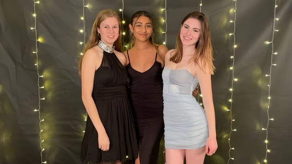 Tres estudiantes en ropa formal posan frente a un fondo de luces brillantes en el campus del Centennial Collegiate.