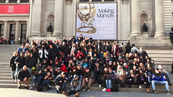 Un gran grupo de estudiantes se reúne frente al edificio de la Centennial Regional High School con el banner 'Making Miracles'.