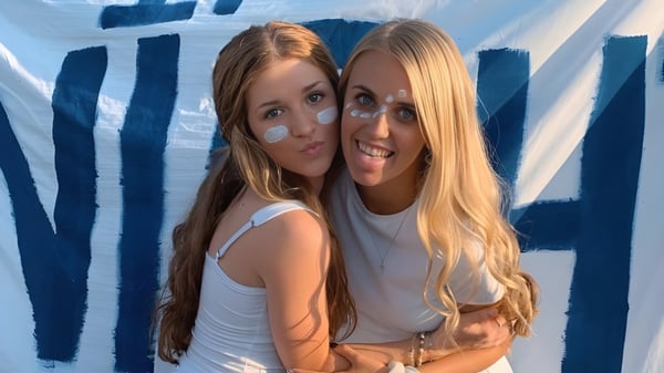 Dos estudiantes de la Central Catholic Jr.-Sr. High School se abrazan frente a un fondo abstracto azul y blanco.