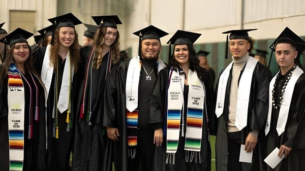 Un grupo de graduadas y graduados en togas se encuentra juntos frente a un fondo sencillo en el campus de la Central Methodist University.