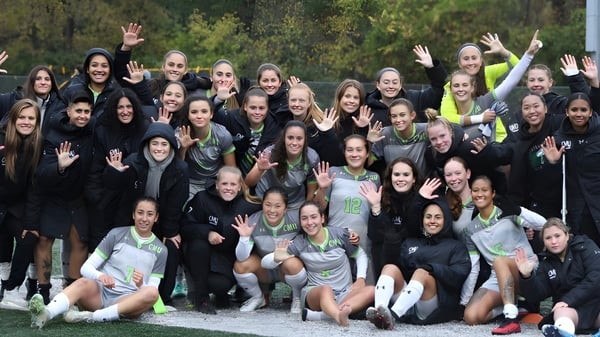 Un grupo de jóvenes mujeres en ropa deportiva saluda al aire libre frente a un fondo boscoso en el campus de la Central Methodist University.