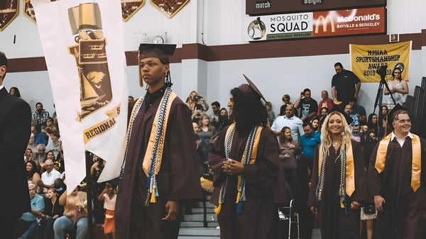 Estudiantes de la Central Regional High School en togas de graduación están de pie frente a un McDonald's con pancartas.