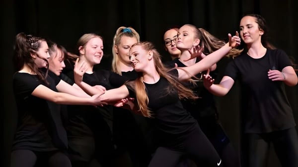 Un grupo de jóvenes mujeres vestidas de negro realizan una actuación en el escenario del Central Southland College.