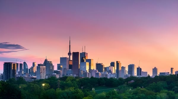 Un vibrante paisaje urbano con rascacielos al atardecer, rodeado de vegetación verde, representado sin referencia directa a la Central Toronto Academy.