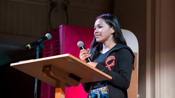 Una joven habla en el podio frente a un fondo rojo en el campus de la Central Toronto Academy.