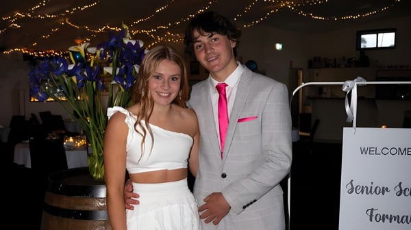 Una joven pareja está en un evento en el campus de la Central Yorke School frente a un fondo decorado con luces y flores.