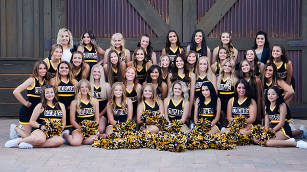Un grupo de animadoras con pompones posan juntas frente a un edificio de madera en el terreno de la Chaffey Joint Union High School District.