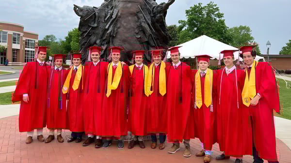 Un grupo de graduados en togas rojas y amarillas está frente a una gran estatua de bronce en el campus de la Chaminade College Preparatory School.