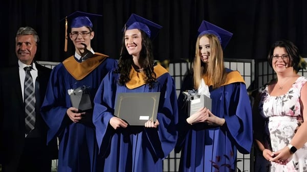 Graduados de la Char-Lan District High School están en togas azules en el escenario con docentes al fondo.