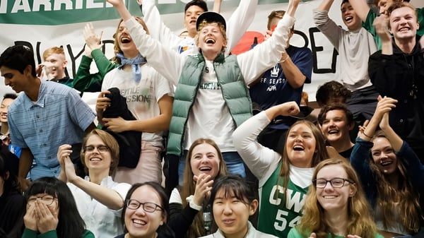 Un gran grupo de estudiantes de la Charles Wright Academy celebra juntos con los brazos en alto en un interior.