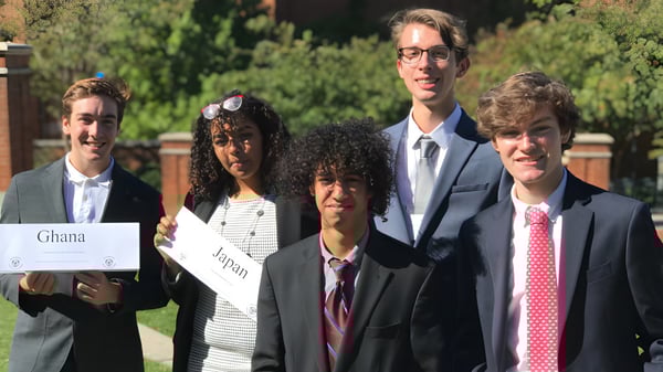Un grupo de estudiantes de las Charlotte-Mecklenburg Schools está junto afuera en un campo con árboles al fondo.