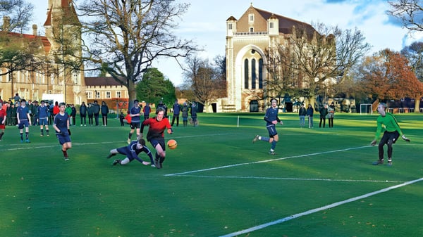 Un grupo de estudiantes juega al rugby en el campo de la Charterhouse School frente a un edificio histórico.
