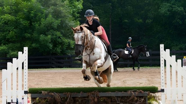Una mujer vestida de montar monta un caballo moteado en el terreno de la Chatham Hall School sobre un salto en un patio exterior.