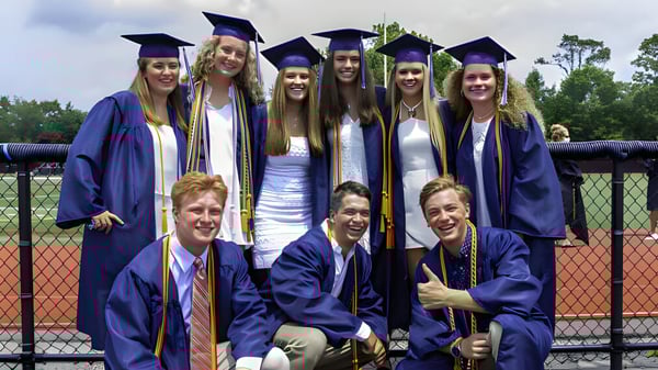 Un grupo de graduados de la Chatham Kent Secondary School está frente a un campo deportivo cercado.