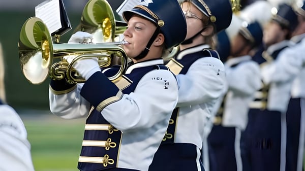 Un miembro de la banda marcial de Chelsea High School toca un instrumento de metal en uniforme blanco y azul.