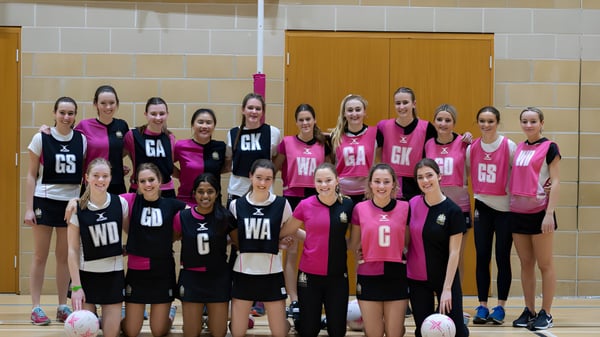 Un grupo de jóvenes jugadoras de netball del Cheltenham College posan en el gimnasio con suelo y paredes de madera.