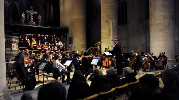 La orquesta del Cheltenham College toca en un escenario en una gran catedral frente a un público.